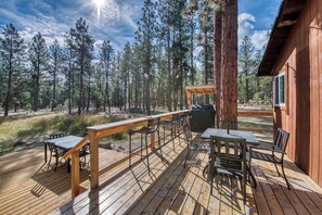 Eine Holzterrasse mit Gartenmöbeln, einem Grill und Blick auf einen Wald.