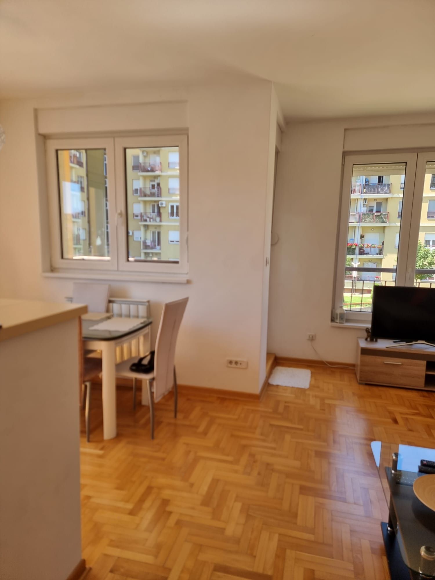 Quarto com mesa de jantar, cadeiras, aparador e janela com vista para um edifício.