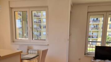 Quarto com mesa de jantar, cadeiras, aparador e janela com vista para um edifício.