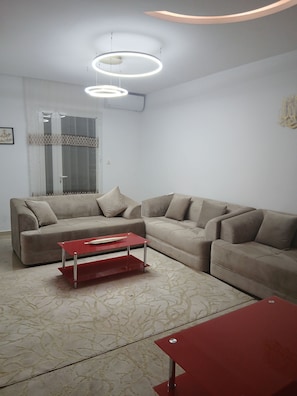 A modern living room with a sofa set, a red coffee table, and a patterned rug.