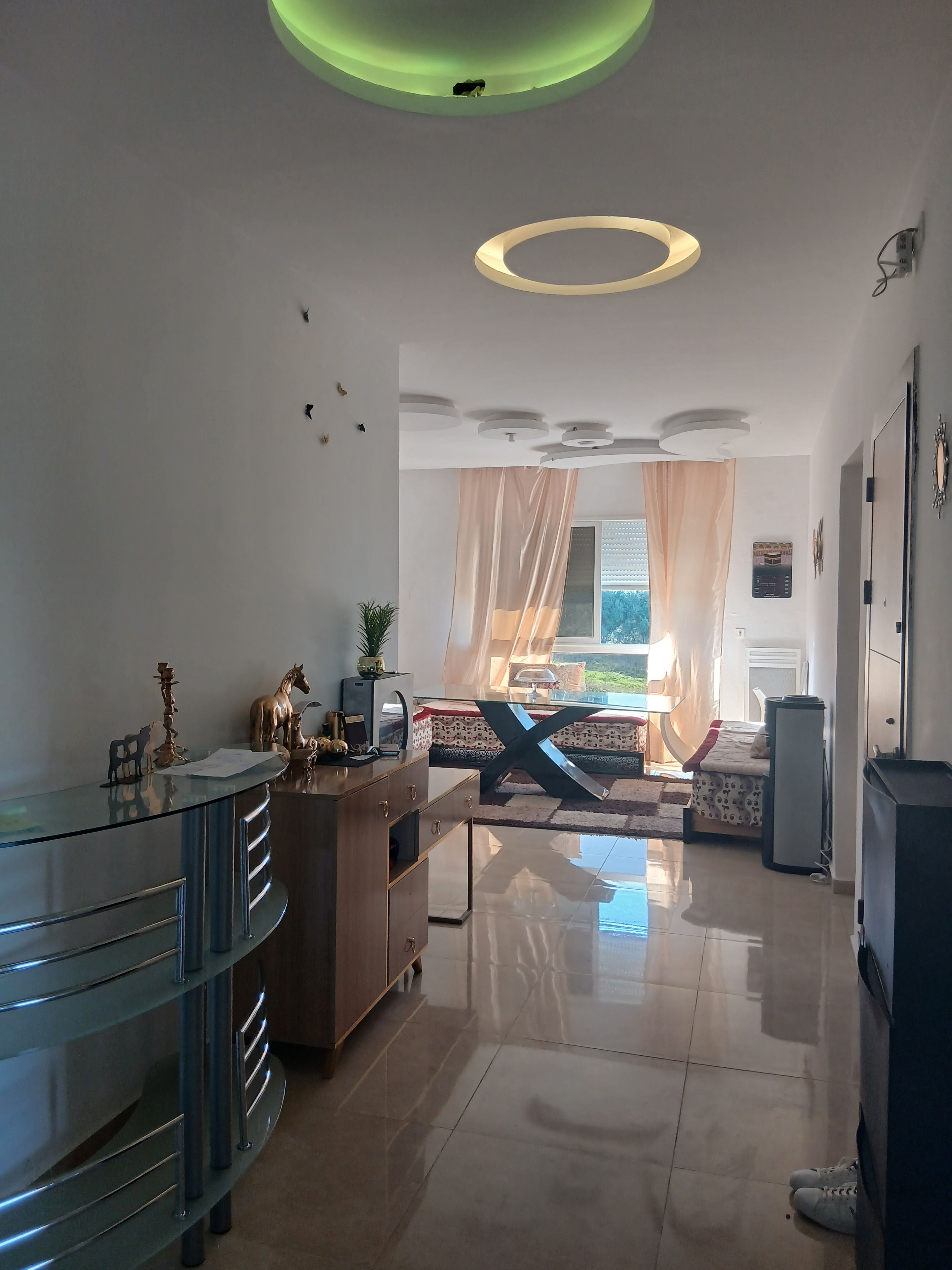 Ein modernes Interieur mit einem Glastisch, einem Bett mit Vorhängen und einer Decke mit runden Leuchten.