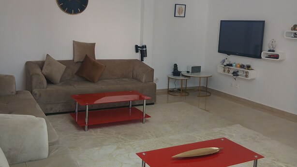 A modern living room with a sofa, a red coffee table, a flat-screen TV, and a ceiling light fixture. - A lovely, beautiful view (Nefza)