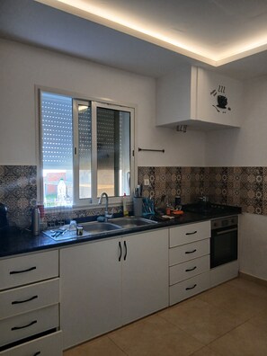 Une cuisine moderne dotée d’une grande fenêtre, de meubles blancs et d’un plan de travail noir.