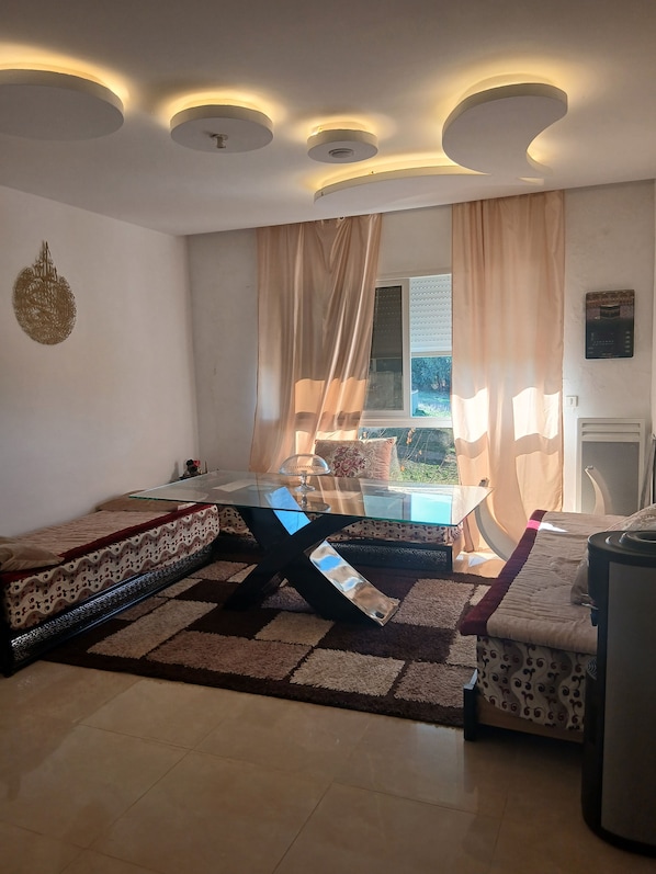 A living room with a glass-top coffee table, a sofa, and a bed with patterned bedding.