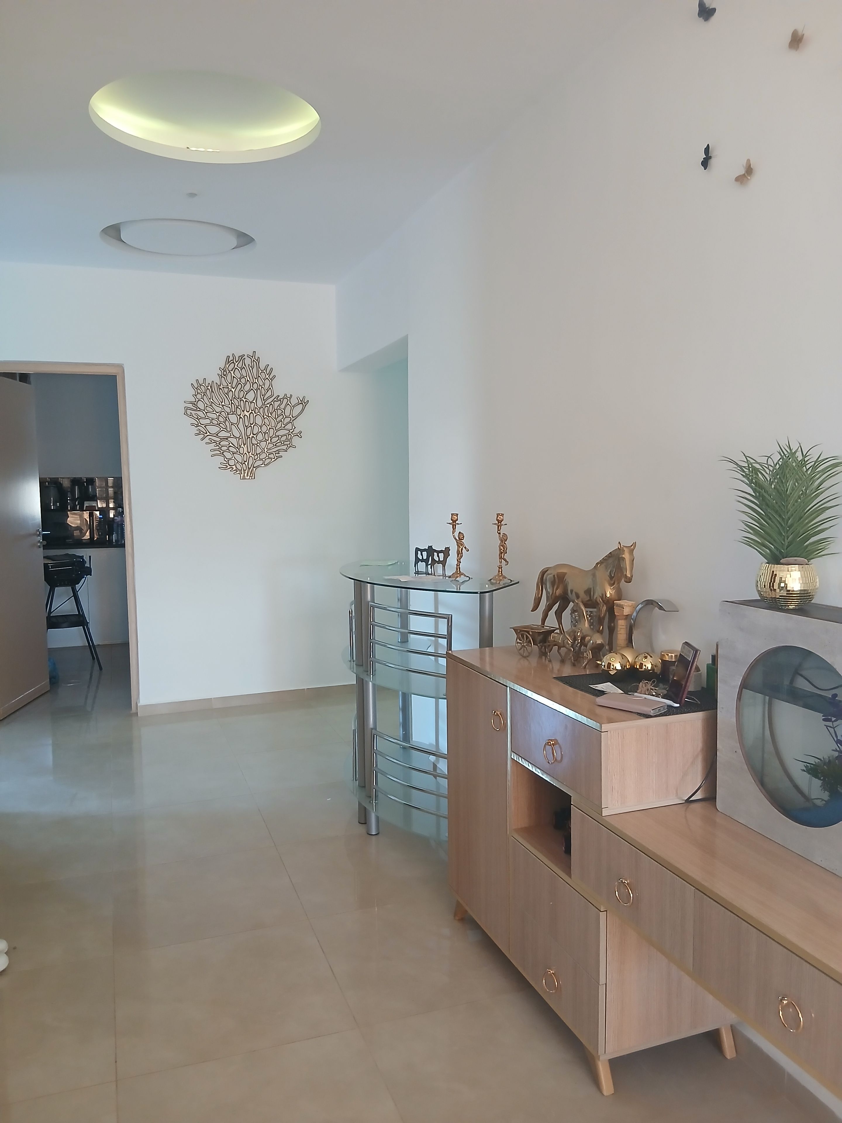 A modern living room with a glass coffee table, wooden cabinet, and decorative items including a fish tank and wall art.
