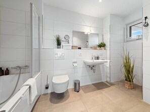 Ein modernes Badezimmer mit Badewanne, Toilette, Waschbecken und einem großen Spiegel.