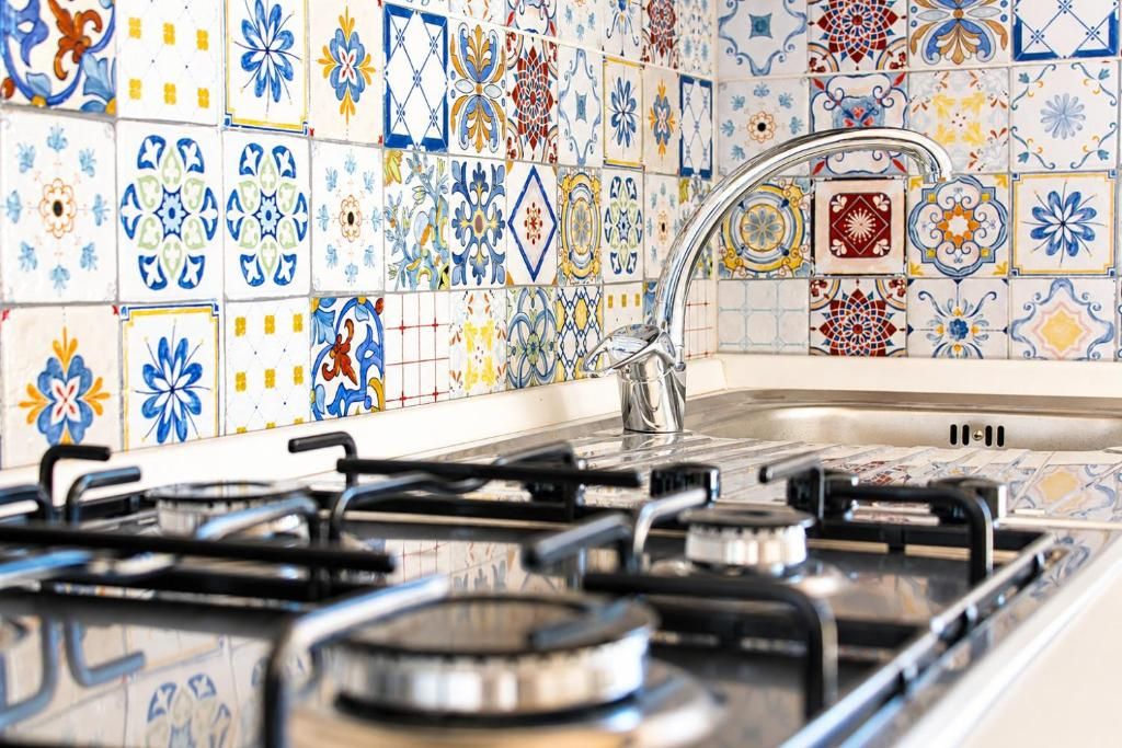 A kitchen with a gas stove, a sink, and a tiled backsplash with various patterns.