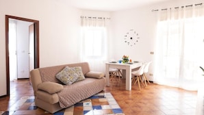 Una sala de estar con un sofá, una mesa de comedor con sillas, un reloj de pared y una puerta.