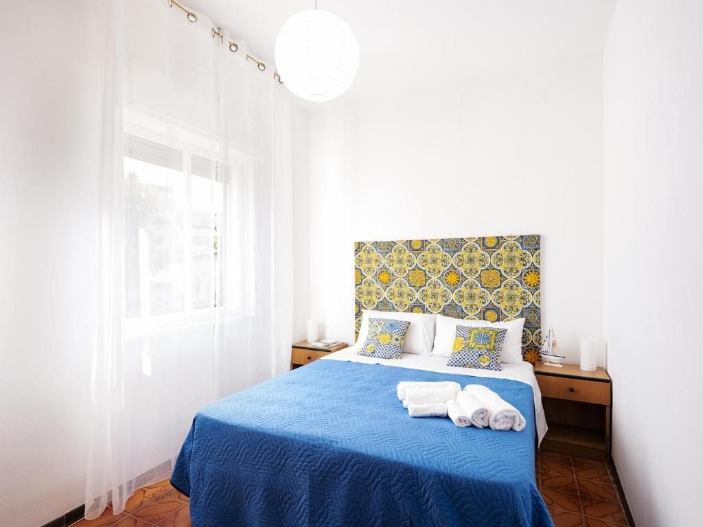 A hotel room with a bed, a nightstand, a window with sheer curtains, and a patterned headboard.
