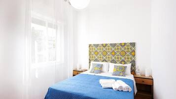 A hotel room with a bed, a nightstand, a window with sheer curtains, and a patterned headboard.