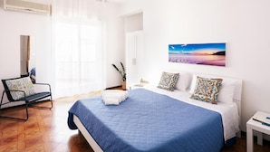Un dormitorio con cama, una silla, una mesita de noche y un cuadro en la pared.