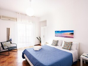 A bedroom with a bed, a chair, a bedside table, and a painting on the wall. - Appartamenti Abate Limoncello (Alcamo)