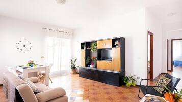 A modern living room with a sofa, a coffee table, a TV stand with cabinets, and a dining area with a table and chairs.