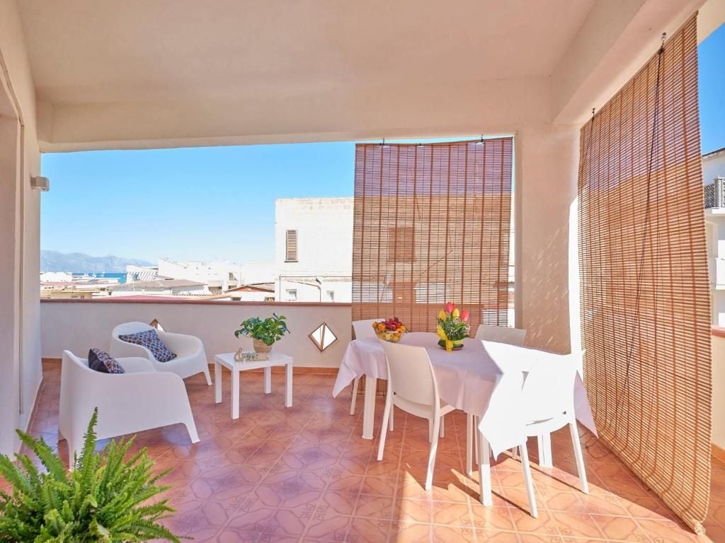A balcony with white furniture, a table with a vase of flowers, and a view of buildings and mountains.