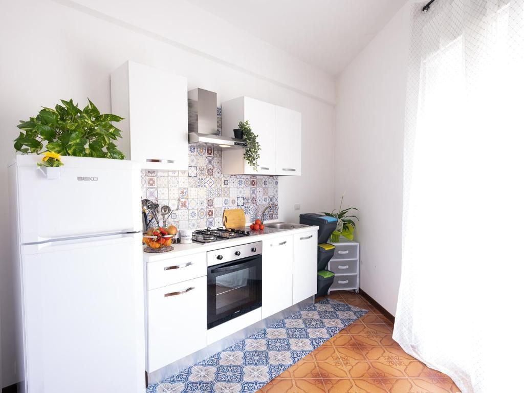 A compact kitchen with white cabinets, a stove, and a refrigerator. There is a tiled backsplash and a patterned floor.