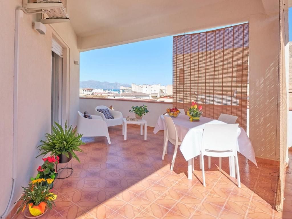 Un balcón con una mesa y sillas, plantas en macetas y vistas a edificios y montañas.