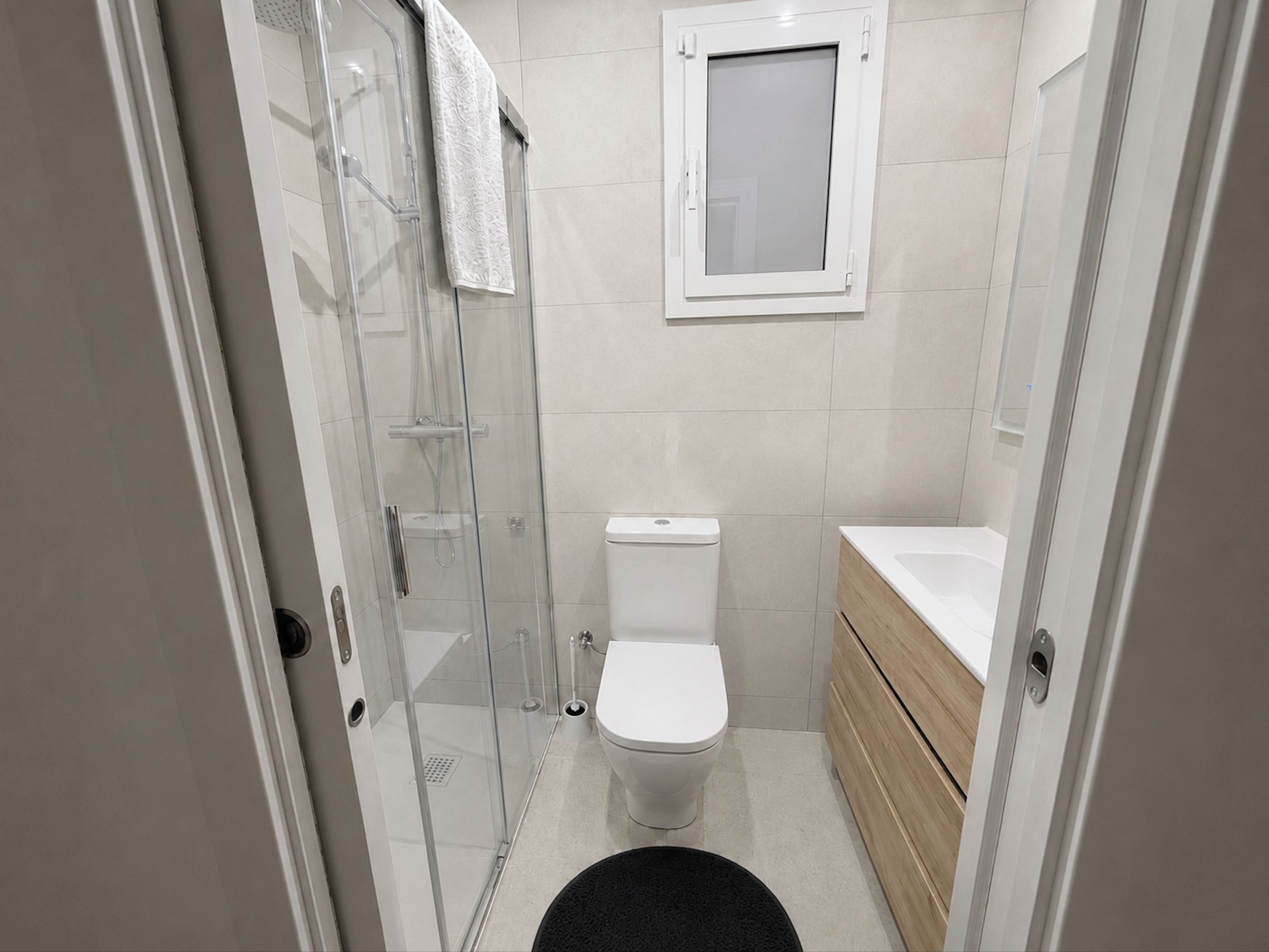 Een badkamer met een douchecabine van glas, een toilet en een houten wastafelmeubel met een wastafel.