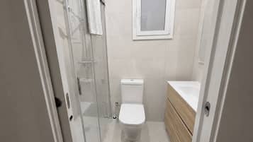 Een badkamer met een douchecabine van glas, een toilet en een houten wastafelmeubel met een wastafel.
