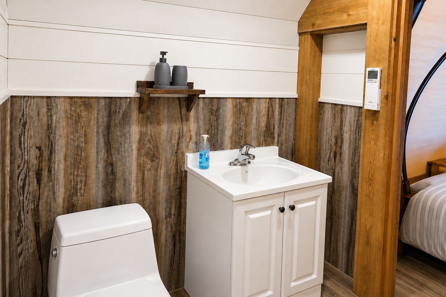 Een badkamer met een wit toilet, een witte wastafel met een houten kastje en een houten wand.
