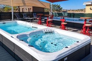 A rooftop pool area with two hot tubs, lounge chairs, and red tables. - High Chaparral RV & MHC (Casa Grande)