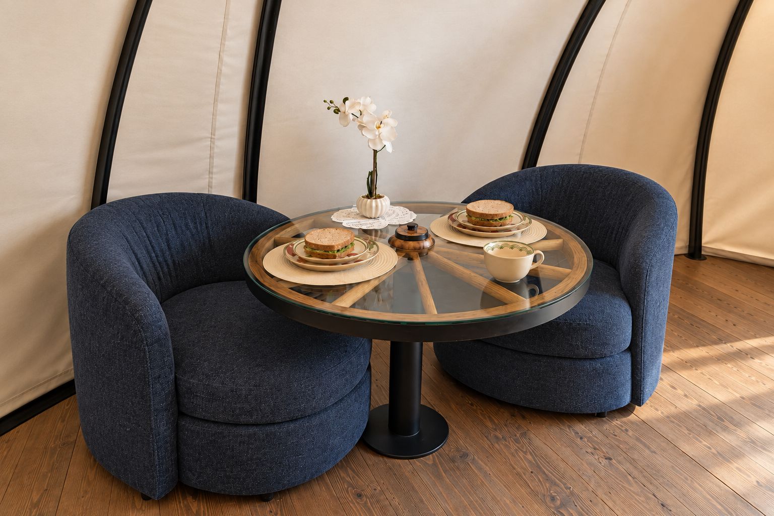 A round glass table with two chairs, a vase with white flowers, and a sandwich on the table.