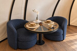 Ein runder Glastisch mit zwei Stühlen, einer Blumenvase mit weißen Blumen und einem Sandwich darauf.