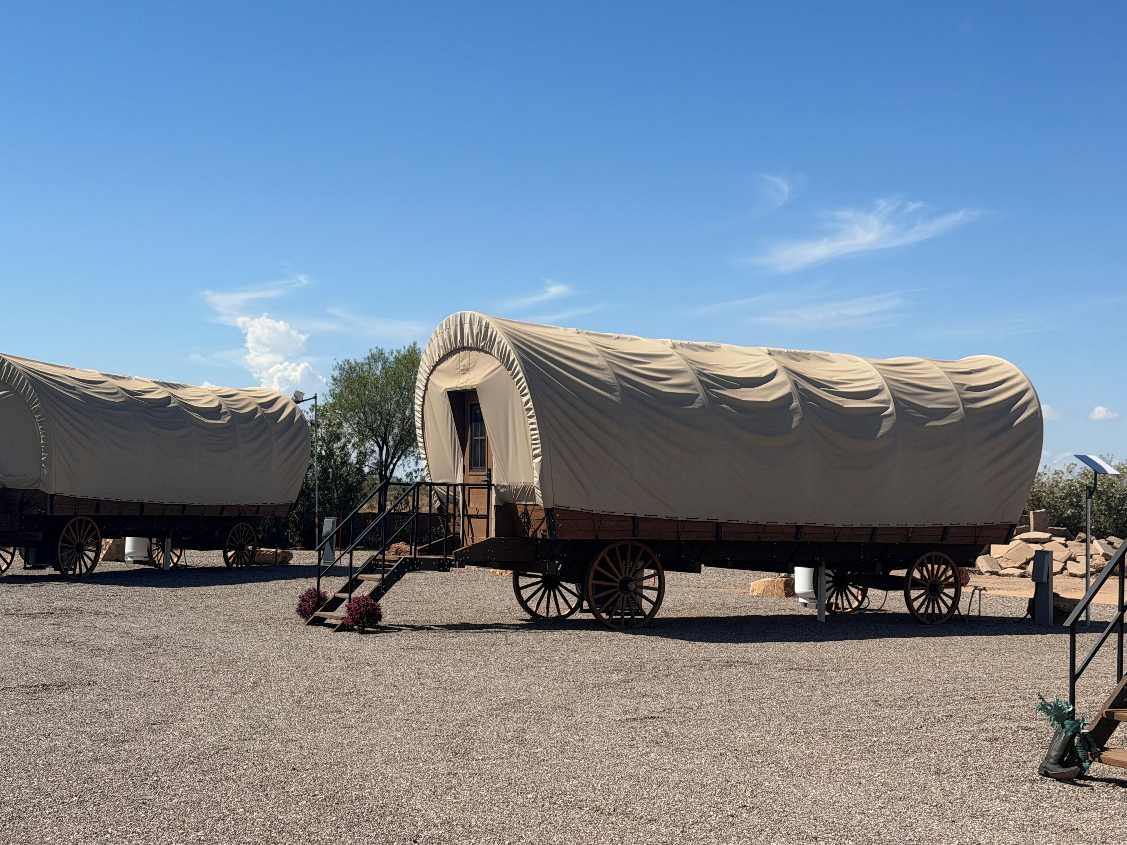 A covered wagon with a door and steps, parked on a gravel surface.