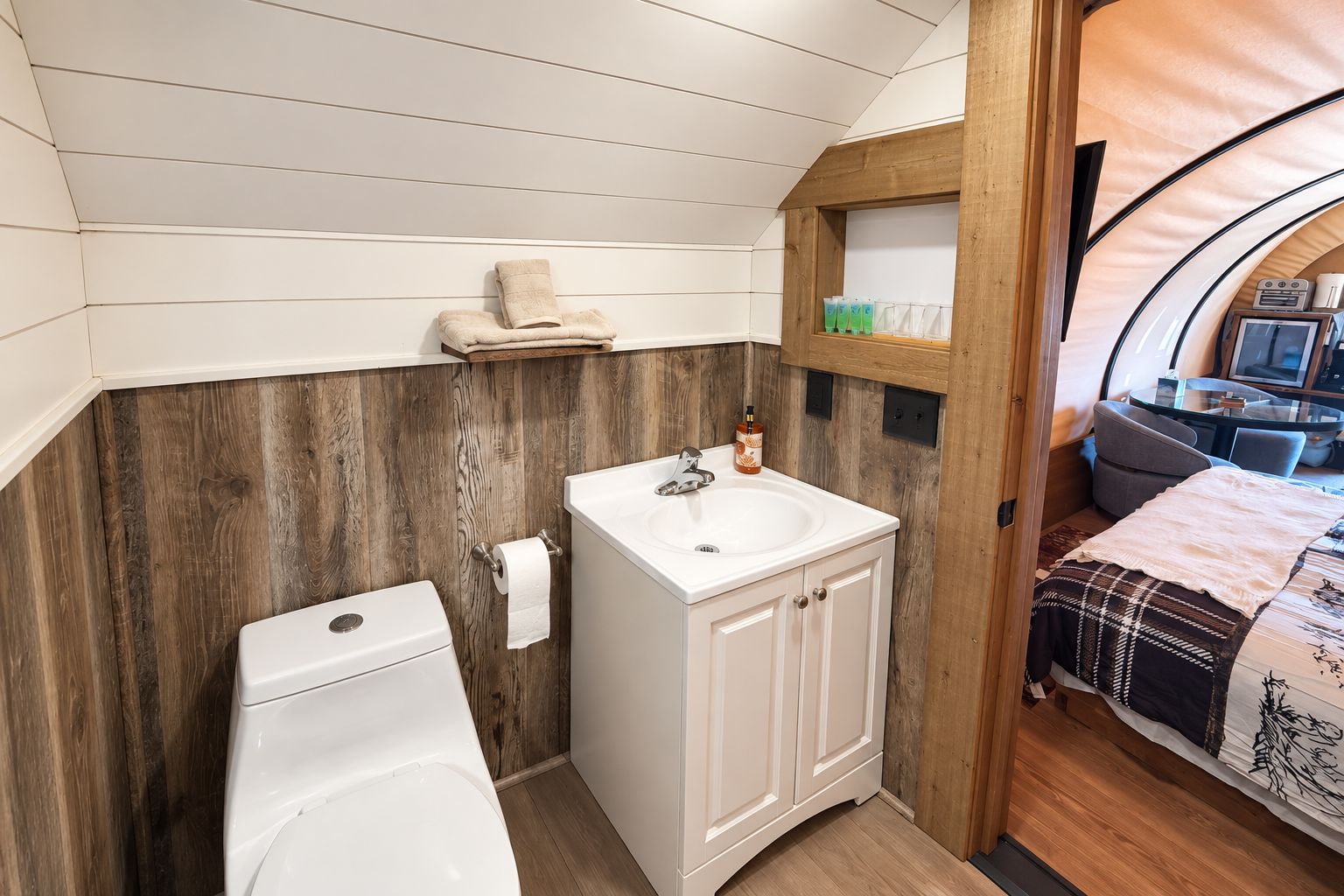 A compact bathroom with a white sink, toilet, and wooden wall paneling.