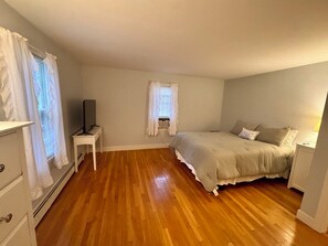 A bedroom with a bed, a television on a stand, a window with curtains, and a radiator. - Beach Days, Family Nights, and Cape Cod Memories! (Yarmouth)