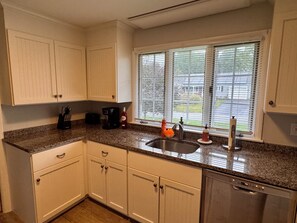 A kitchen with white cabinets, a granite countertop, a coffee maker, a sink, and a dishwasher. - Beach Days, Family Nights, and Cape Cod Memories! (Yarmouth)