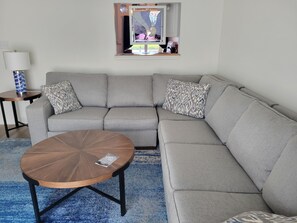A living room with a grey sectional sofa, a round wooden coffee table, and a small side table with a lamp. - Charming townhome/condo walk to Yacht Club & Ocean Pines Marina (Berlin)