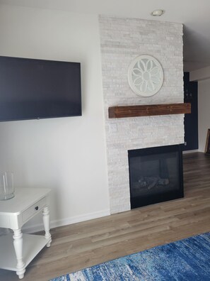 Ein modernes Wohnzimmer mit Kamin aus weißem Backstein, einem Wand-Fernseher und Holzboden.