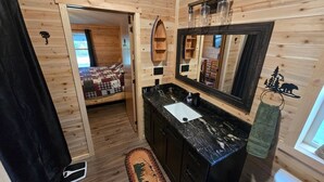 A wooden cabin interior with a bathroom, a bed, and a view of the outside. - Trailside Lodge - Where Adventure Begins! (Shingleton)