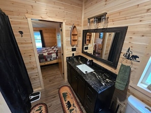 A wooden cabin interior with a bathroom, a bed, and a view of the outside. - Trailside Lodge - Where Adventure Begins! (Shingleton)