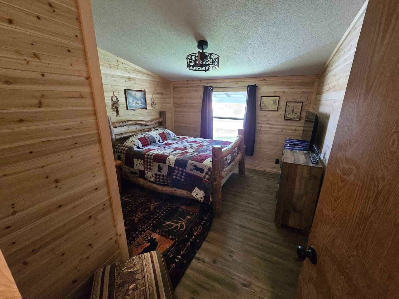 Ein Zimmer mit Holzwänden, einem Bett, einem Schreibtisch und einem Deckenventilator.