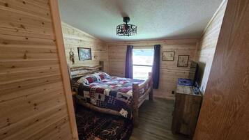 Ein Zimmer mit Holzwänden, einem Bett, einem Schreibtisch und einem Deckenventilator.
