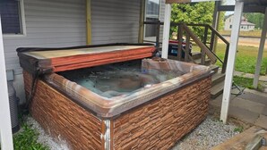 A hot tub with a stone exterior, a covered area with steps, and a house in the background. - Trailside Lodge - Where Adventure Begins! (Shingleton)