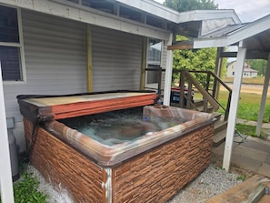 A hot tub with a stone exterior, a covered area with steps, and a house in the background. - Trailside Lodge - Where Adventure Begins! (Shingleton)
