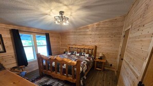 A wooden-paneled room with a bed, a wooden table, and a window. - Trailside Lodge - Where Adventure Begins! (Shingleton)