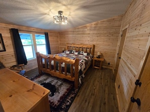 A wooden-paneled room with a bed, a wooden table, and a window. - Trailside Lodge - Where Adventure Begins! (Shingleton)