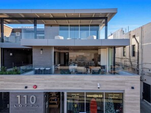 Un bâtiment moderne à la façade vitrée, doté d’une terrasse sur le toit avec des sièges, et d’une devanture portant l’inscription « 110 LOFTS », où sont exposés des œuvres d’art et des vêtements de créateurs locaux.