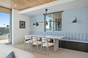 A modern kitchen with a marble countertop, four chairs, a bench, and pendant lighting. - Newport Beach | Luxury Condo | Steps to Sand (Newport Beach)