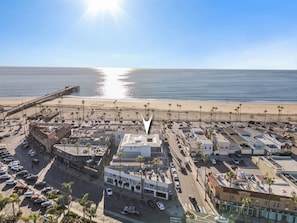 An aerial view of a coastal town with a beach, parking lots, and buildings. - Newport Beach | Luxury Condo | Steps to Sand (Newport Beach)