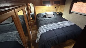 Een compacte slaapkamer in een camper, met stapelbedden, een houten hoofdbord en een klein raam.