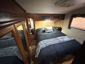 Ein kompaktes Schlafzimmer in einem Wohnmobil mit Etagenbetten, einem Holz-Kopfteil und einem kleinen Fenster.