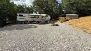 Een recreatievoertuig (rv) geparkeerd op een grindpad, met een houten terras en een gebouw op de achtergrond.
