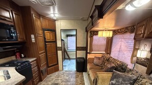 Een ruimtelijk RV-interieur met een kitchenette, een eethoek en een zithoek met een bank en kussens.