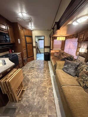 Ein kompaktes Wohnmobil-Interieur mit Küchenzeile, Essbereich und Sitzgruppe, inklusive Sofa und Kissen.