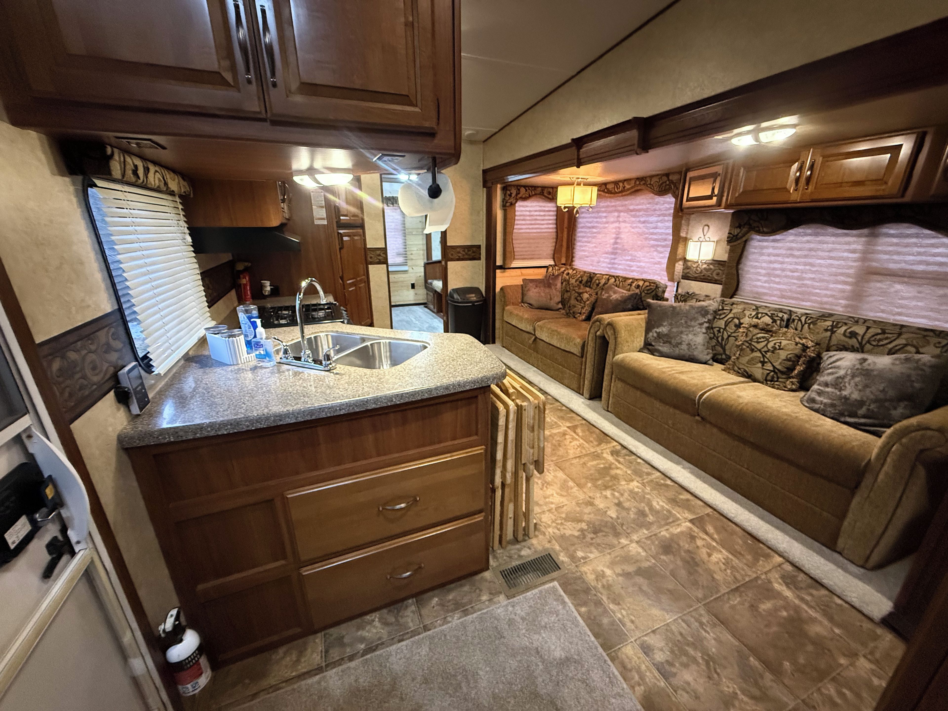 A compact RV kitchen with a sink, countertop, and wooden cabinets.