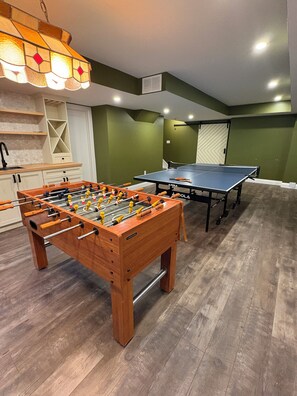 A room with a foosball table, a ping pong table, and a kitchen area with a sink and cabinets. - Creekside Peaceful retreat Near Chicopee, 401 & YKF airport (Kitchener)
